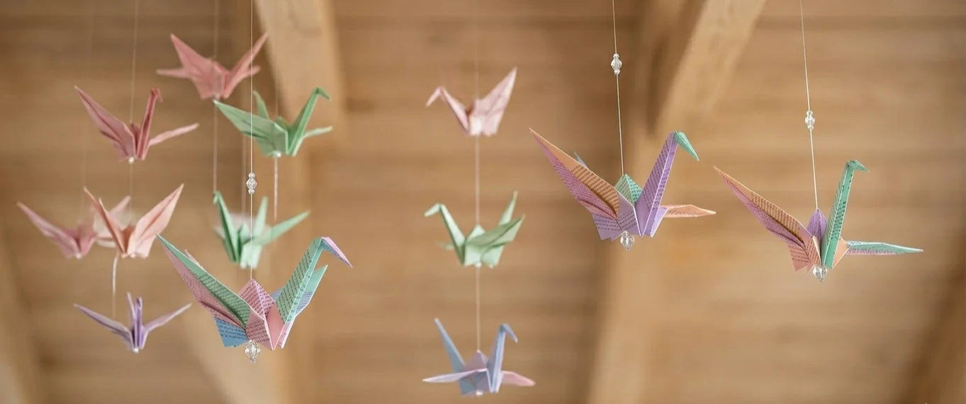 Grullas de origami de colores pastel colgando del techo, imagen representativa de Ales de Paper